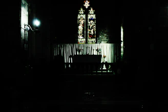 A warm, inviting church interior with soft light highlighting a wooden altar and a stained glass window depicting a wounded heart.