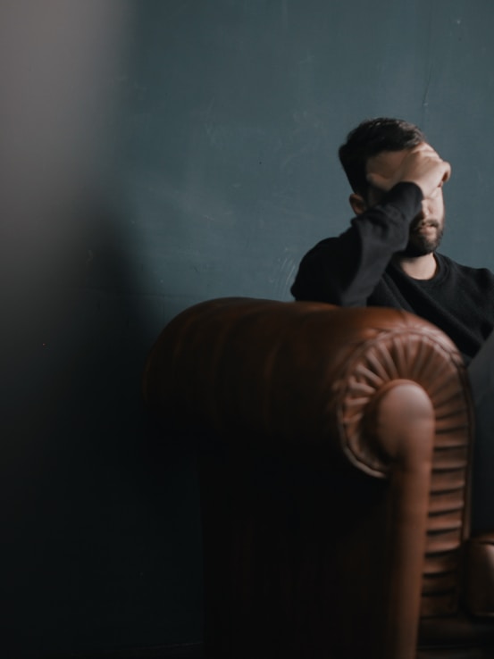 a man holds his head while sitting on a sofa