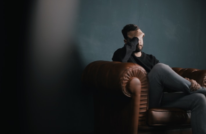 Contemplative man in brown leather armchair, hand covering face in a dark, focused setting
