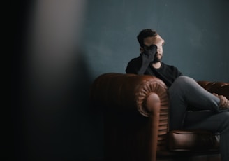 a man holds his head while sitting on a sofa