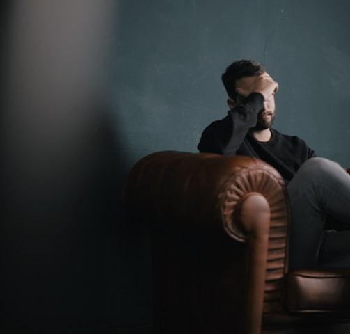 a man holds his head while sitting on a sofa