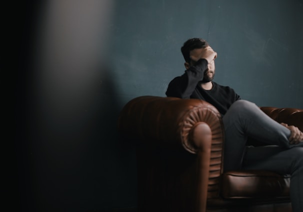 a man holds his head while sitting on a sofa