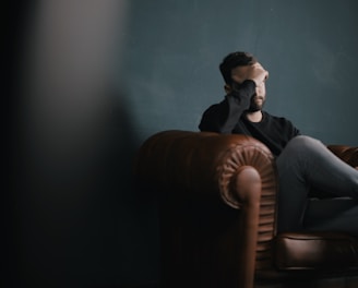 a man holds his head while sitting on a sofa