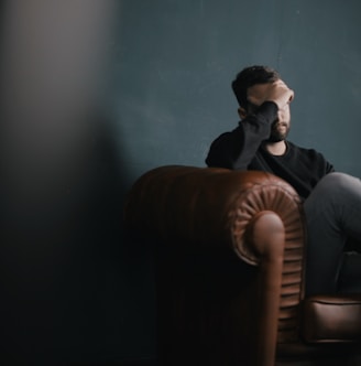 a man holds his head while sitting on a sofa