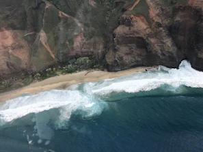A sweeping view of a rugged coastline under a deep blue sky, waves crashing against jagged cliffs.