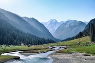 Snow-capped mountains towering over a crystal-clear alpine river winding through a valley.
