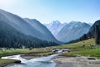 Snow-capped mountains towering over a crystal-clear alpine river winding through a valley.