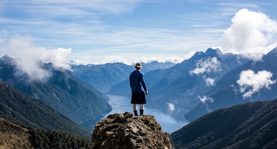 person standing on the top of high rise stone in Kepler Track New Zealand