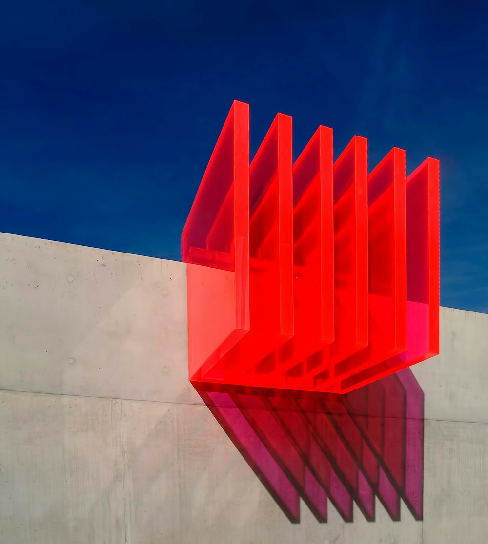 a red sculpture sitting on top of a cement wall
