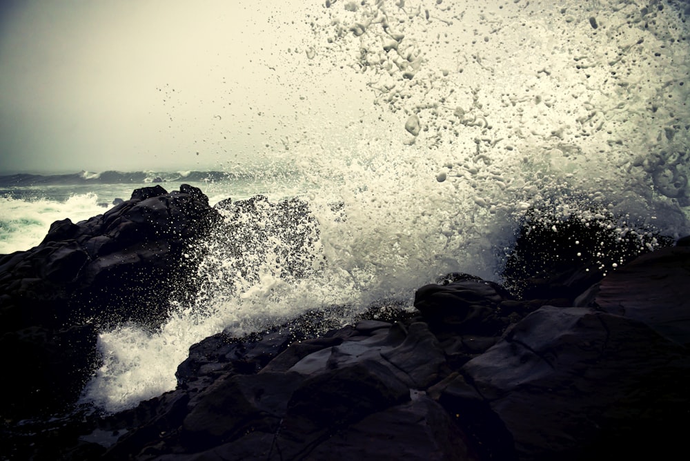 昼間に岩に打ち寄せる海の波のグレースケール写真