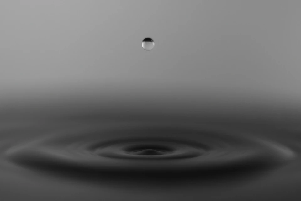 Single drop of water suspended in mid-air above black surface, appearing to move downward
