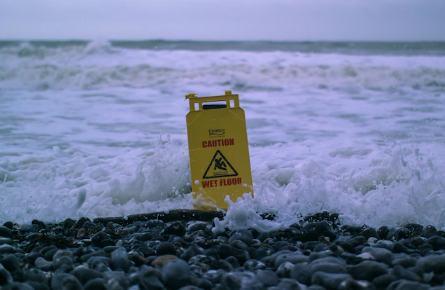 caution wet floor signage on gray rocks in seashore