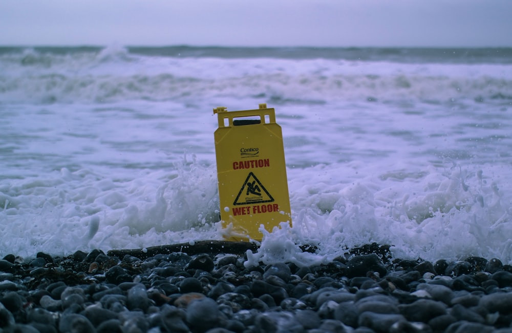 Cuidado: Sinalização de piso molhado em rochas cinzentas em Seashore