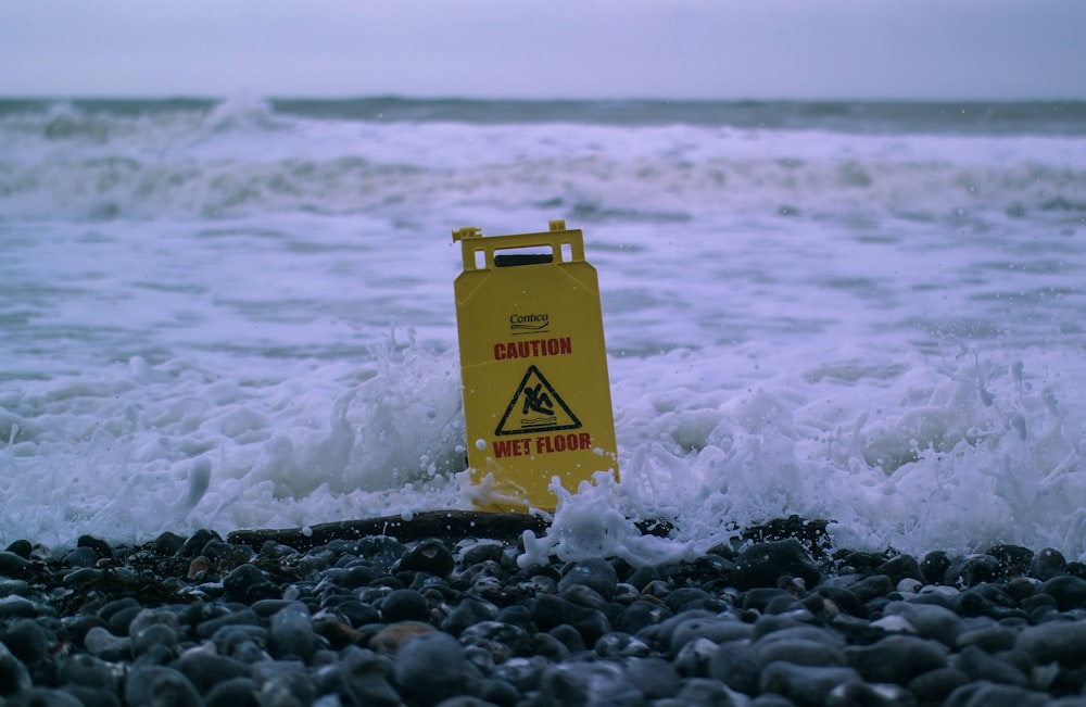 Precaución Señalización de piso mojado en rocas grises en la orilla del mar