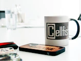 Colorful mugs and mobile cases featuring custom prints arranged on a wooden table.