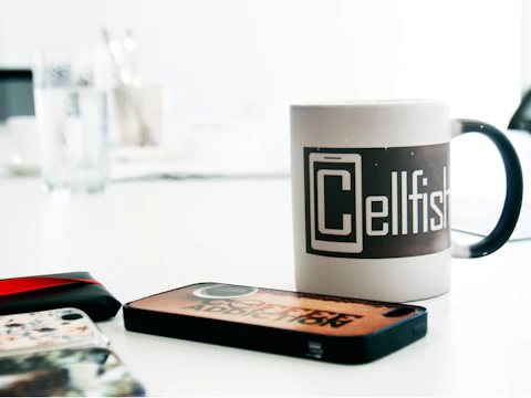 Colorful mugs and mobile cases featuring custom prints arranged on a wooden table.