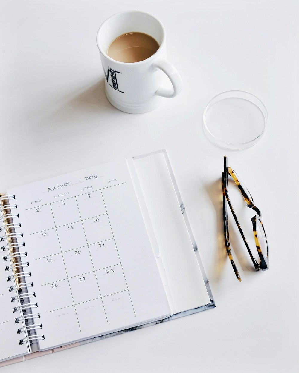 Un libro calendario, un par de vasos y una taza de café sobre una superficie blanca.