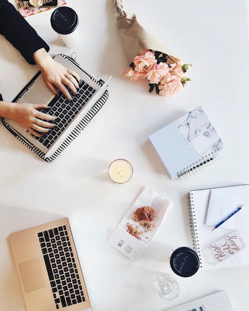 A cozy workspace with a laptop, wedding invitation sketches, and soft pastel decorations.