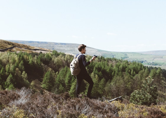A dynamic shot of a hiker capturing a mountain trail with a POV camera, surrounded by lush forest greenery.