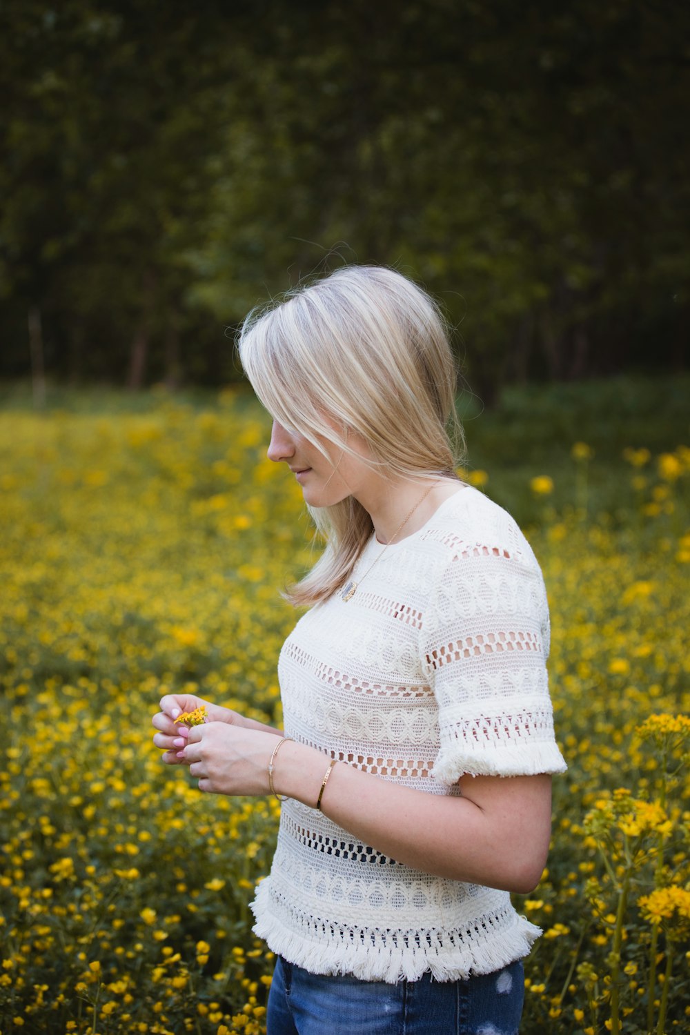 woman wearing white blouse standing and holding yellow flower surrounded with flowers