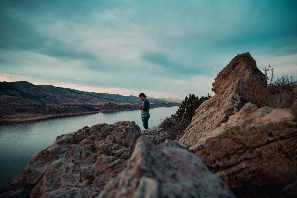 man on brown mountain beside body of water