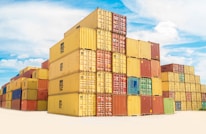 Stacks of colorful shipping containers arranged neatly in a sunny warehouse yard.