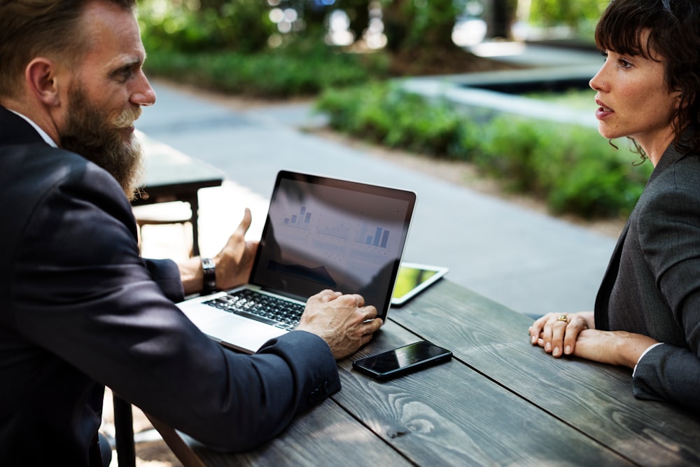 Two businesspeople talking at a table over a laptop with line charts