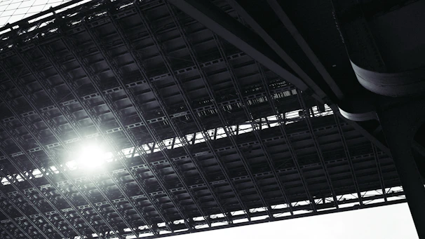 Close-up of a construction blueprint overlaying a steel beam structure under bright site lighting.