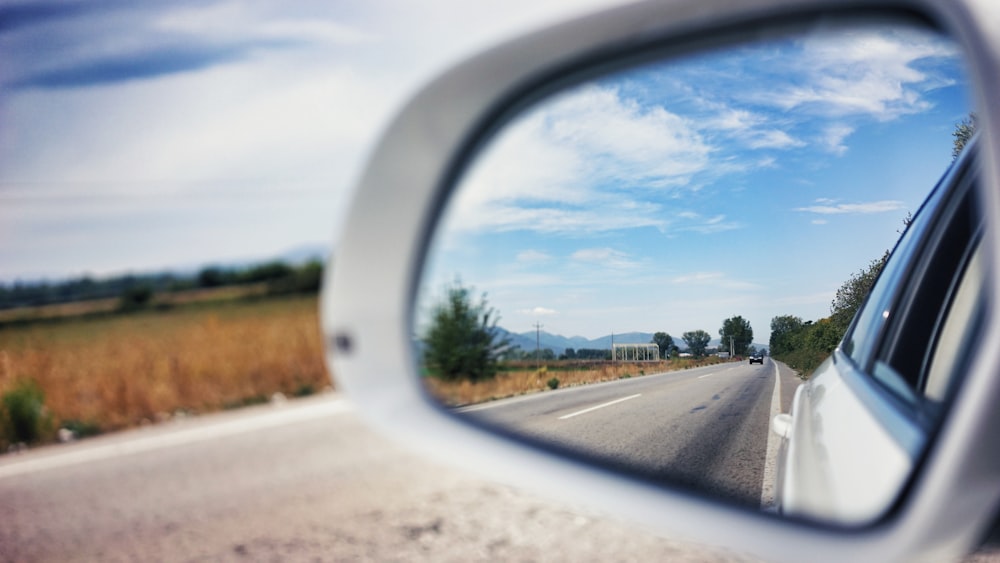 vehicle side mirror viewing car on the road during day