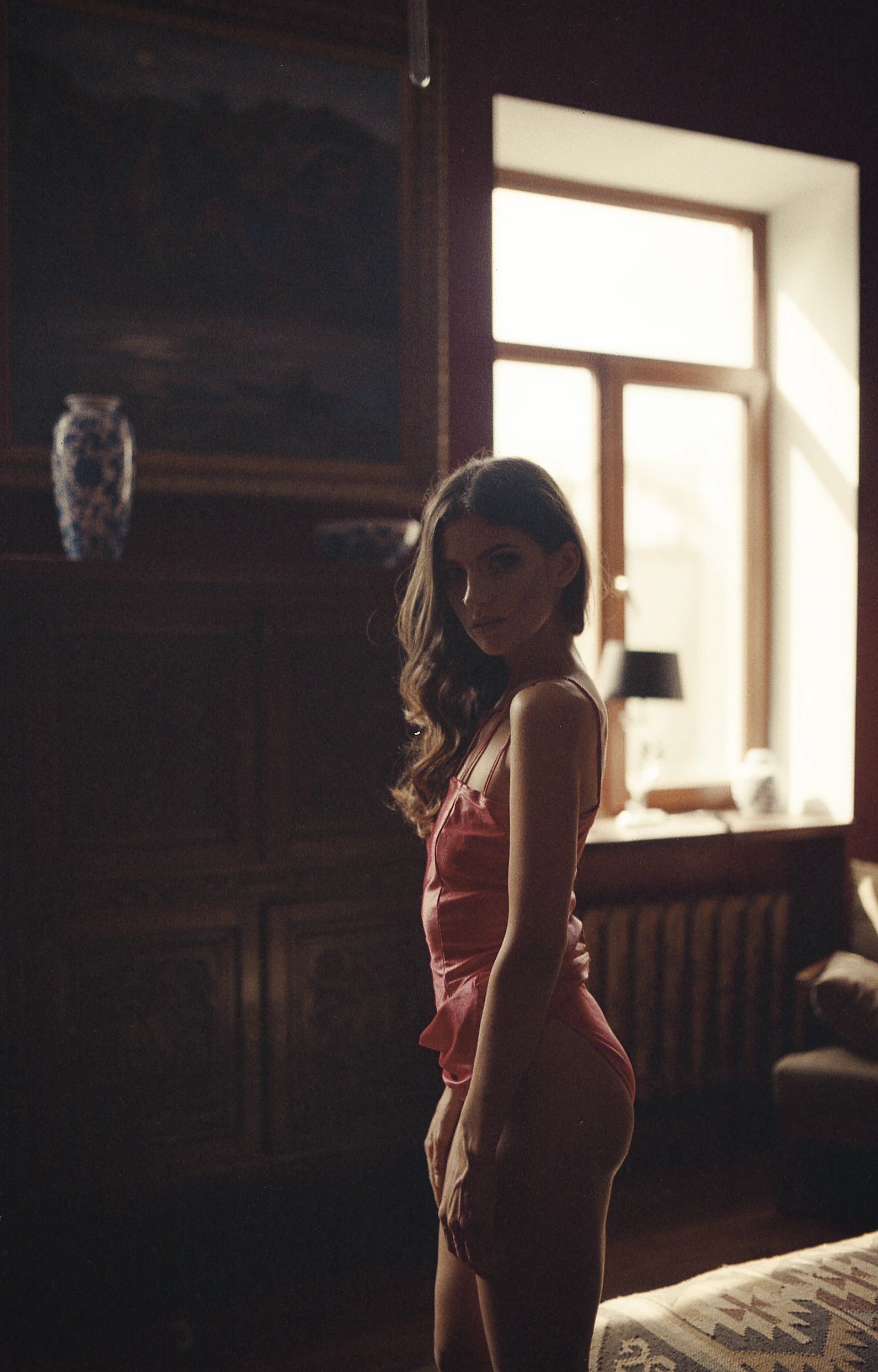 A soft, elegant photo of a confident woman in a light pink workout outfit, smiling gently in a bright, airy room with feminine decor.