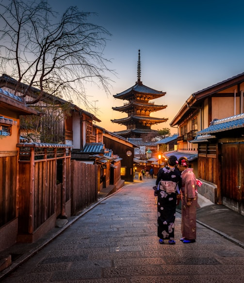 two women in purple and pink kimono standing on street