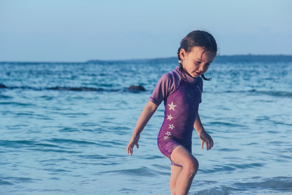 menina no traje de banho roxo em pé perto da costa