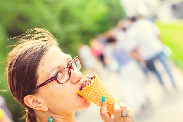 A happy customer enjoying a piece of chocolate outdoors near cacao trees on a sunny day.