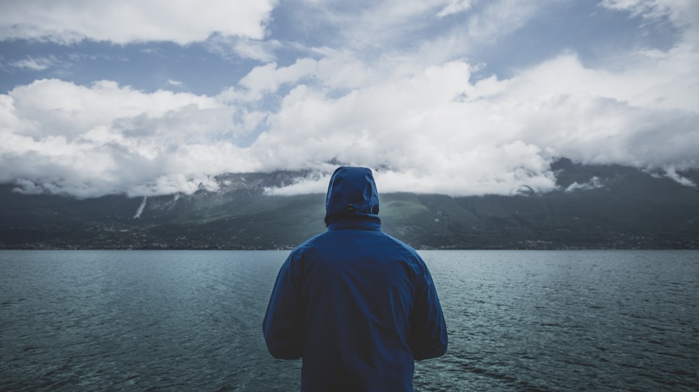 personne portant un chandail à capuchon bleu debout devant un plan d’eau