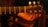 A close-up view of a hand holding the headstock of an acoustic guitar with metallic tuning pegs. The background is dimly lit, creating a warm, intimate ambiance.
