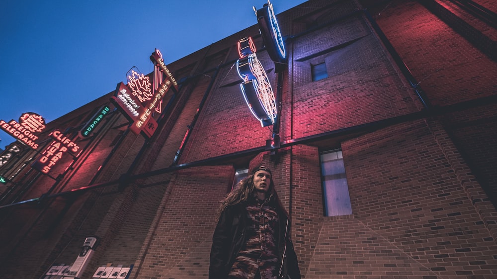 low angle photography of man standing beside gray building