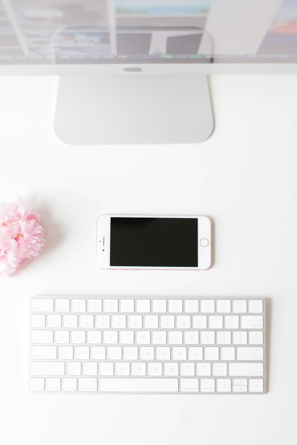 A flatlay image of a smartphone next to a Mac monitor and keyboard.