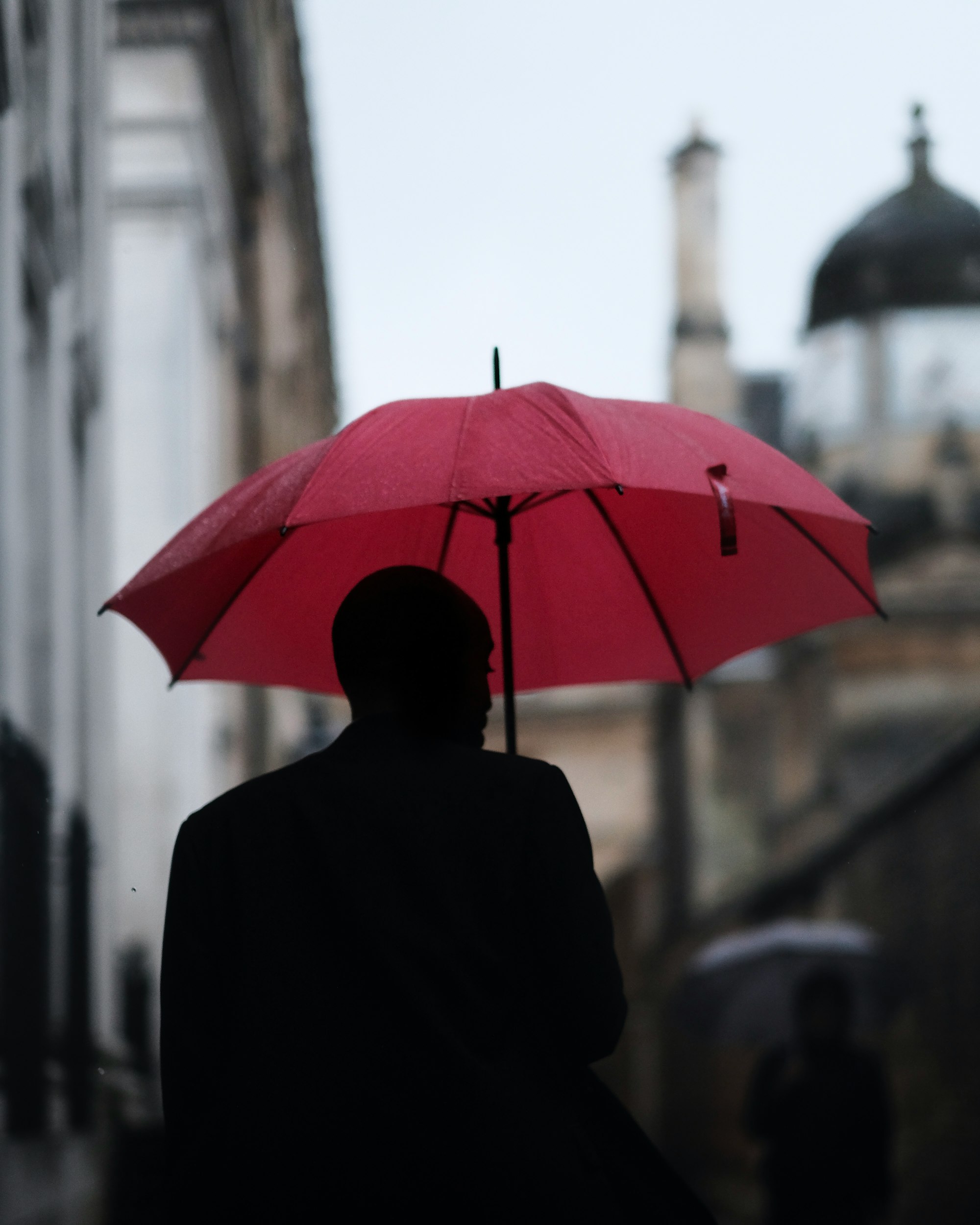 a man with a red umbrella disappears down senate house passage in cambridge uk
