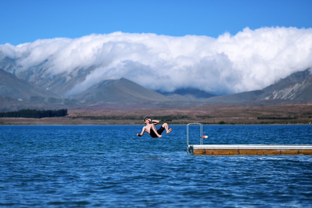 man jumps on body of water holding his nose