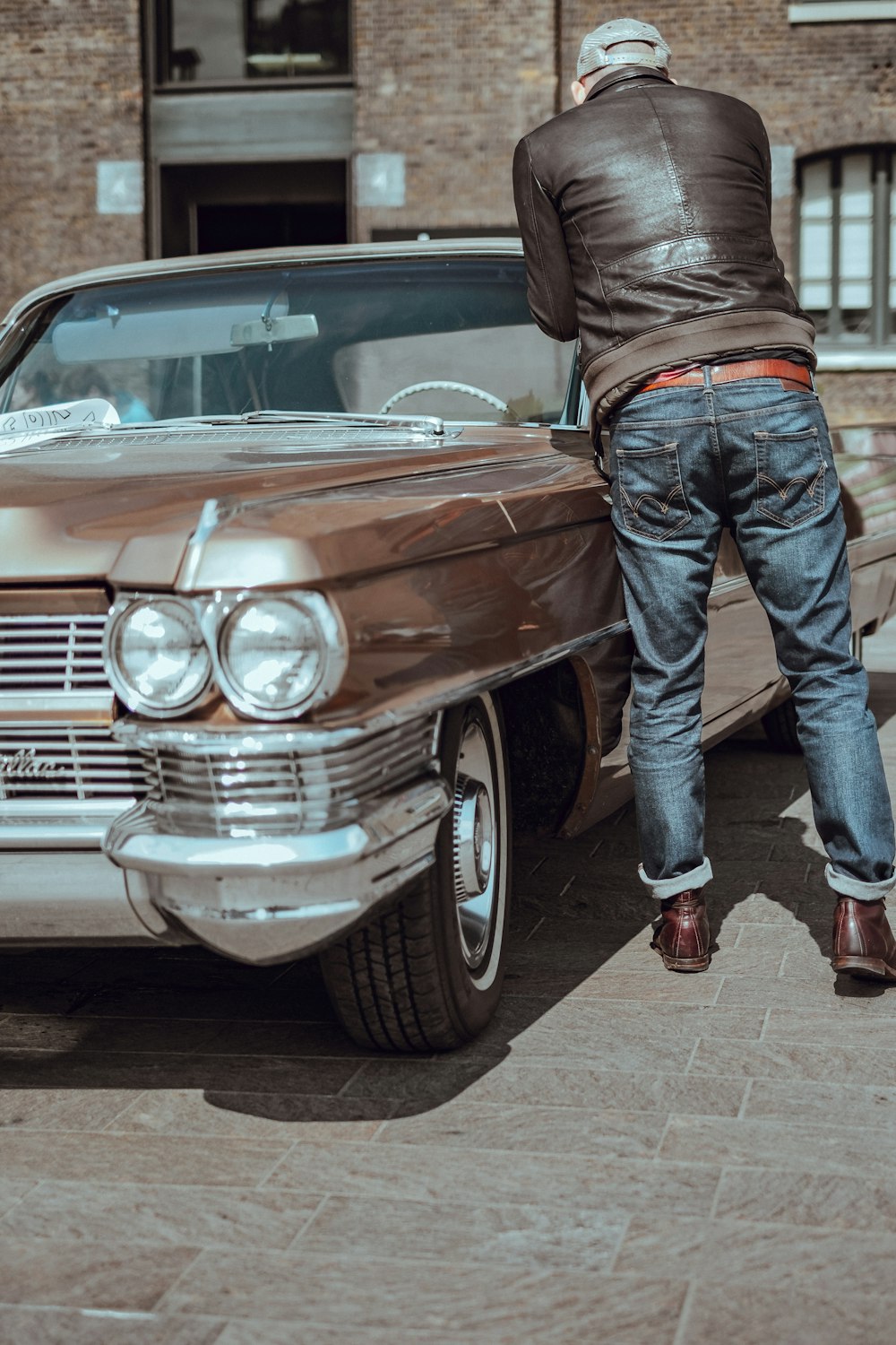 hombre con pantalones de mezclilla azules de pie junto a un automóvil marrón