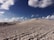 Sand dunes stretch across the horizon under a partly cloudy sky. Several vehicles are visible on the sandy terrain, suggesting an off-road adventure in a desert landscape.
