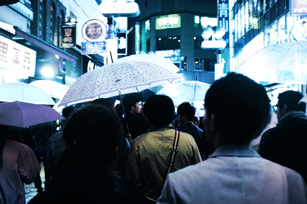 밤에 건물 한가운데서 우산을 쓴 사람들이 도로를 걷고 있습니다.