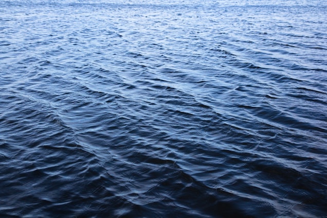 A sleek, translucent water can glowing softly in aqua and navy shades, set against a backdrop of gentle rippling waves.