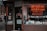 A storefront with various vintage and collectible items displayed. The signage includes a neon sign for a coin and precious metal buying establishment. There is an 'open' sign on the door, which is surrounded by various advertisements and posters. The window features a row of decorative figurines and collectibles.
