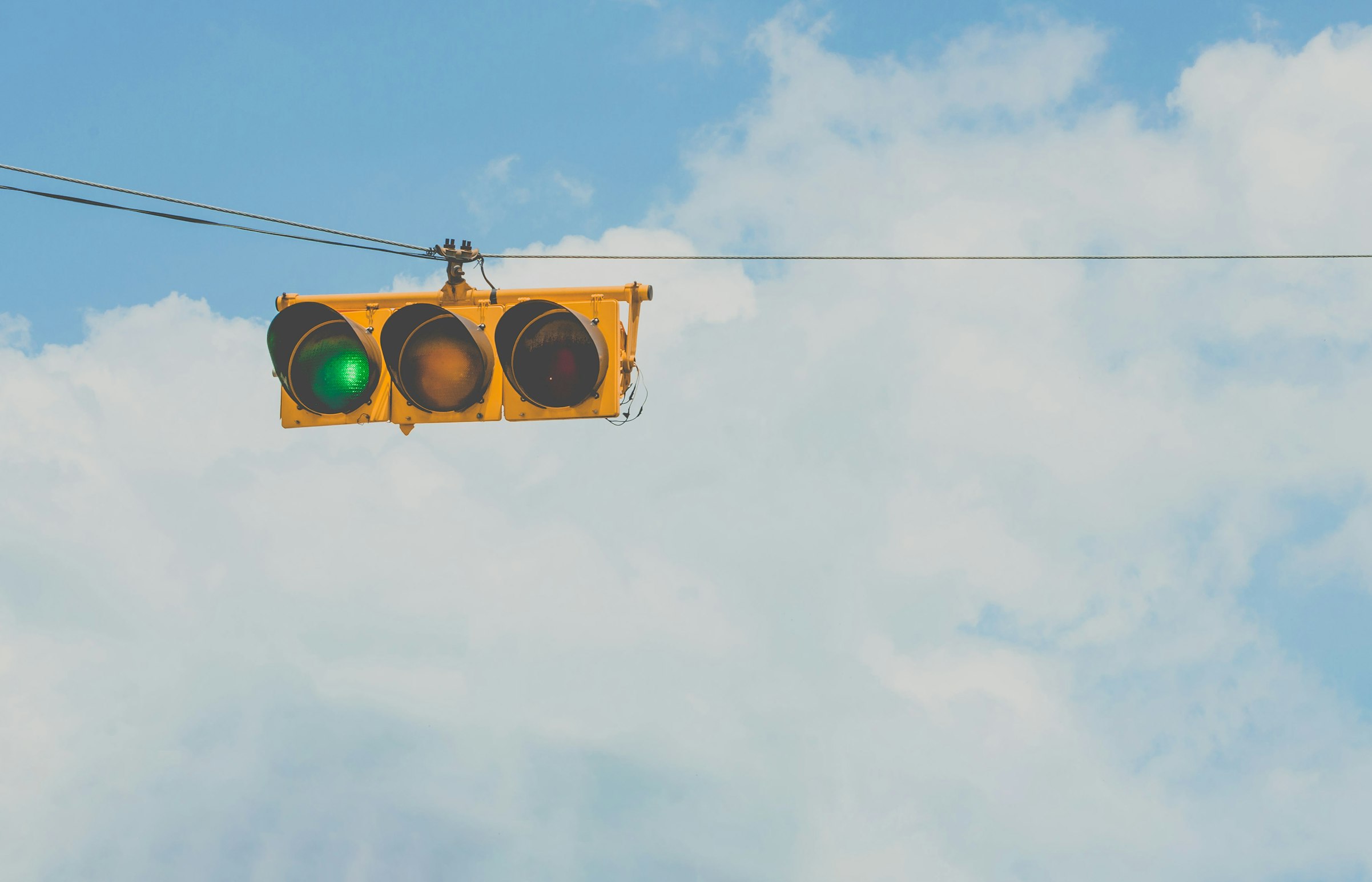 Green traffic light with clouds in the background