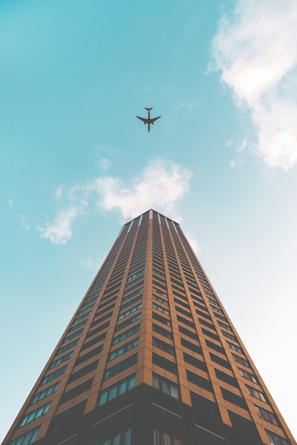 bottom view shot of airplane flying above high rise building