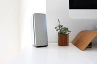 A minimalist desk setup featuring a stylish portable speaker next to a laptop and coffee cup.