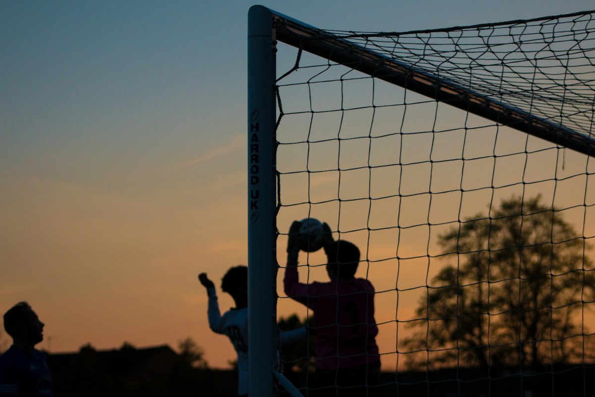 Silhouette d'un gardien de but captant le ballon devant un filet au coucher du soleil