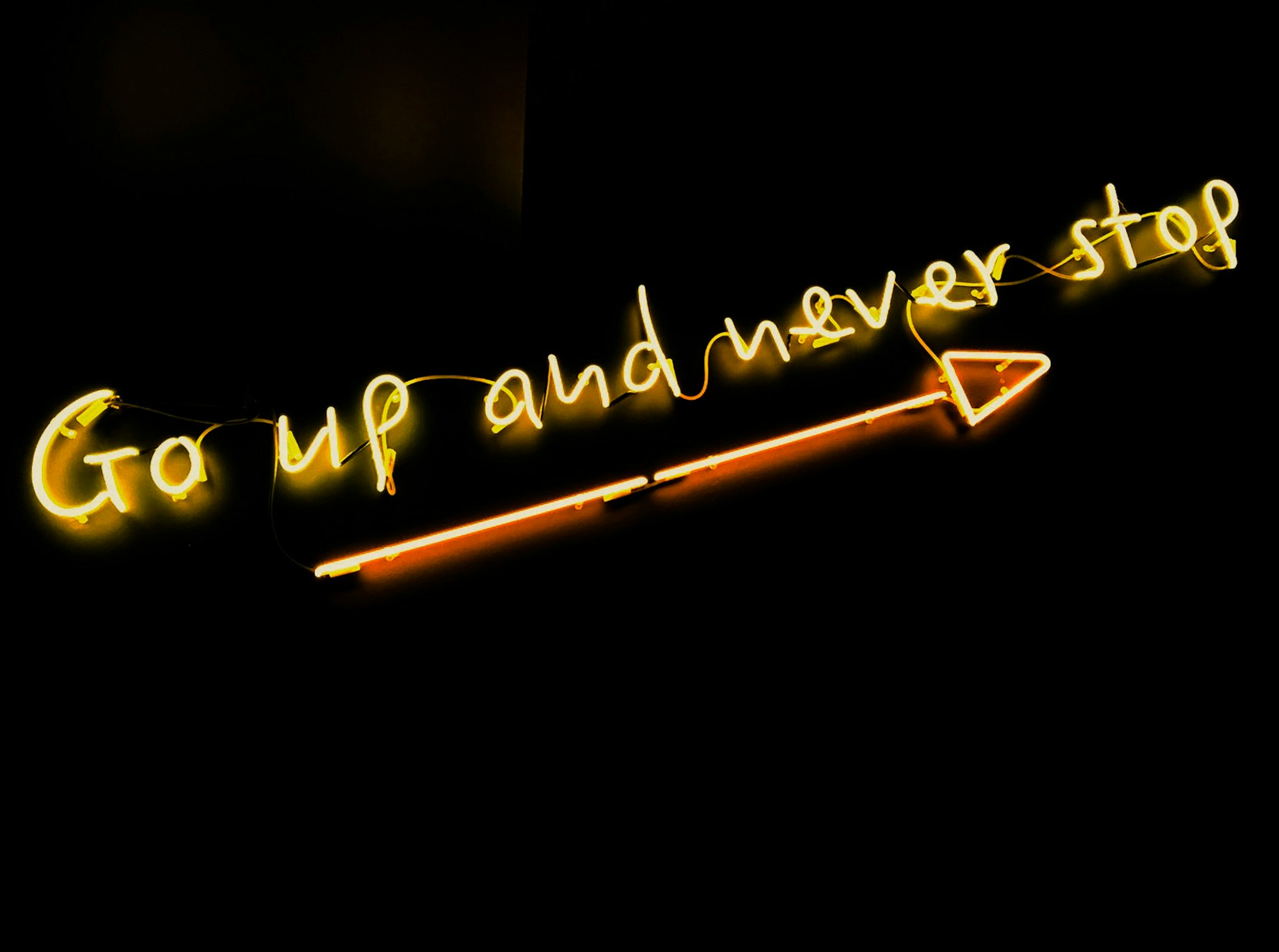 "Go up and never stop" neon sign with an arrow pointing diagonally upwards