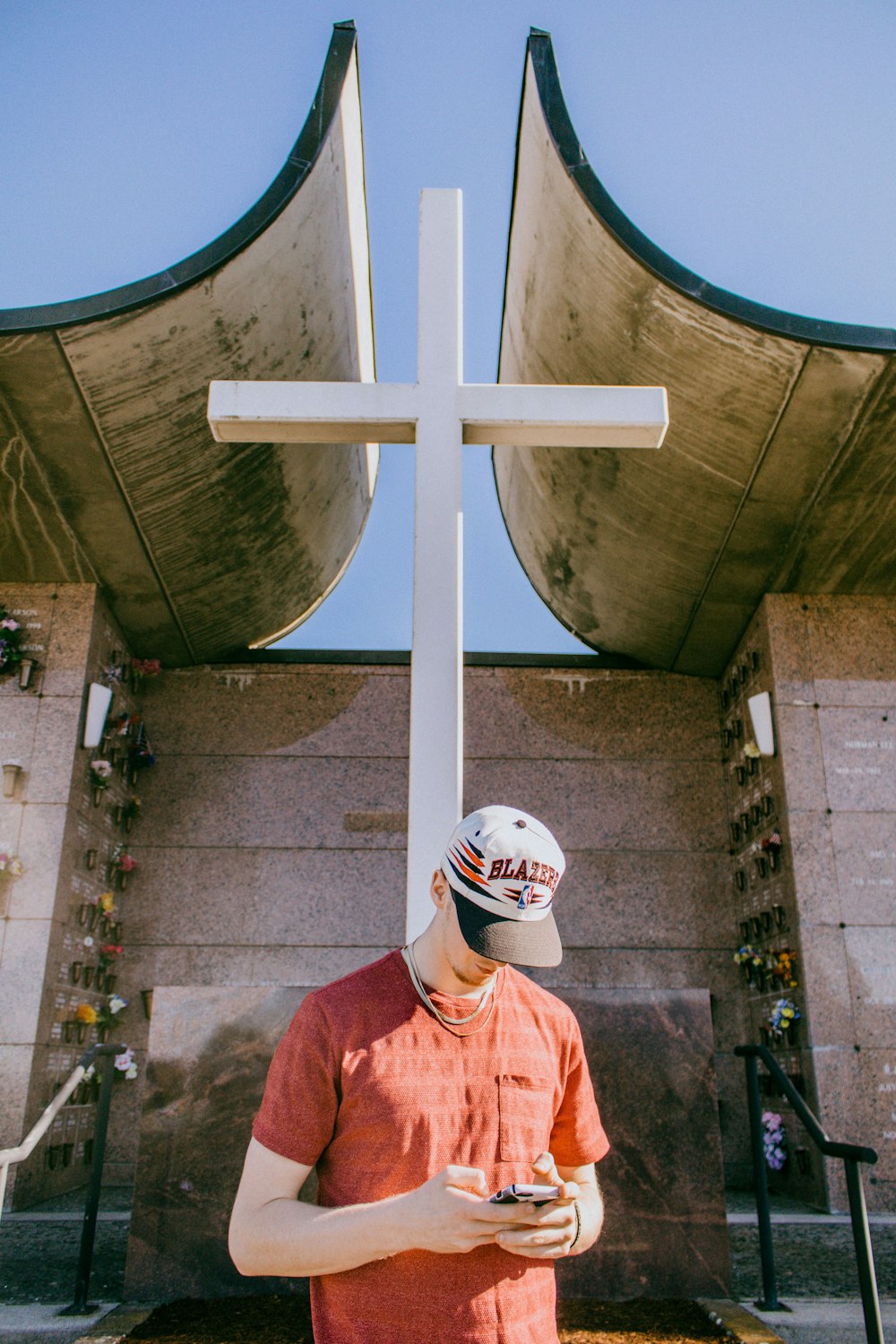 Hombre sosteniendo un teléfono inteligente y de pie cerca de la estatua de la cruz